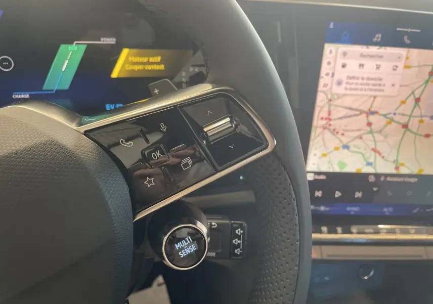 Gros plan sur le volant textile refined et les commandes multifonctions du Renault Rafale 2025 avec écran tactile affichant la navigation.