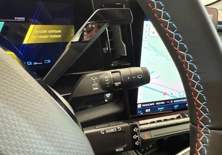 Détail intérieur côté conducteur du levier de vitesses et commandes sur volant cuir noir avec surpiqûres tricolores du Renault Espace hybride.
