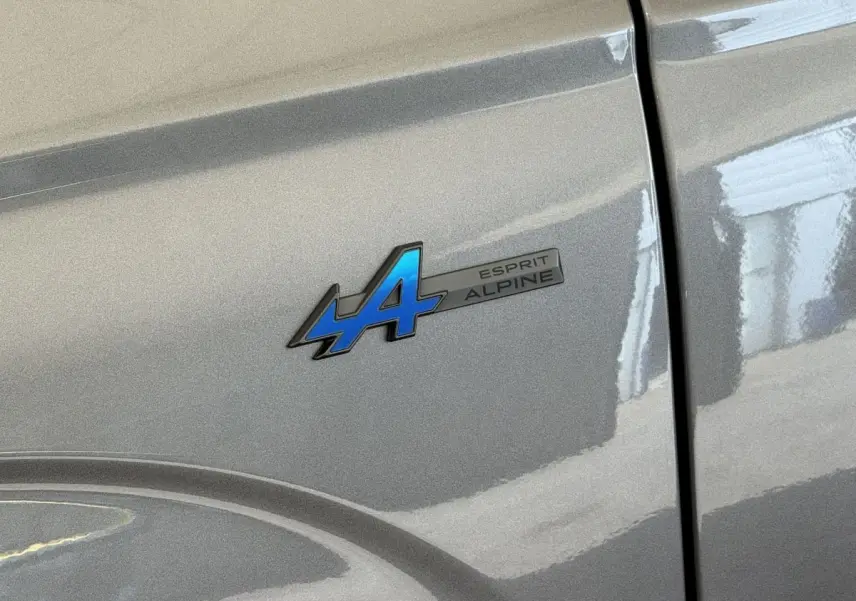 Gros plan sur l'écusson bleu "Esprit Alpine" sur la porte gris foncé d'un Renault Espace hybride 2025.