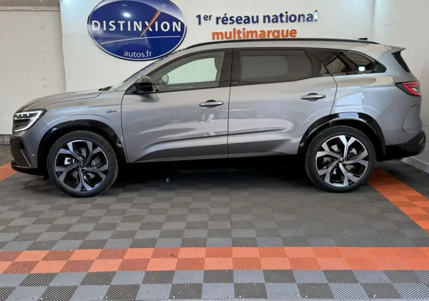 Profil côté gauche d'un Renault Espace esprit Alpine gris foncé, hybride essence, roues alliage et logo Distinxion en arrière-plan.