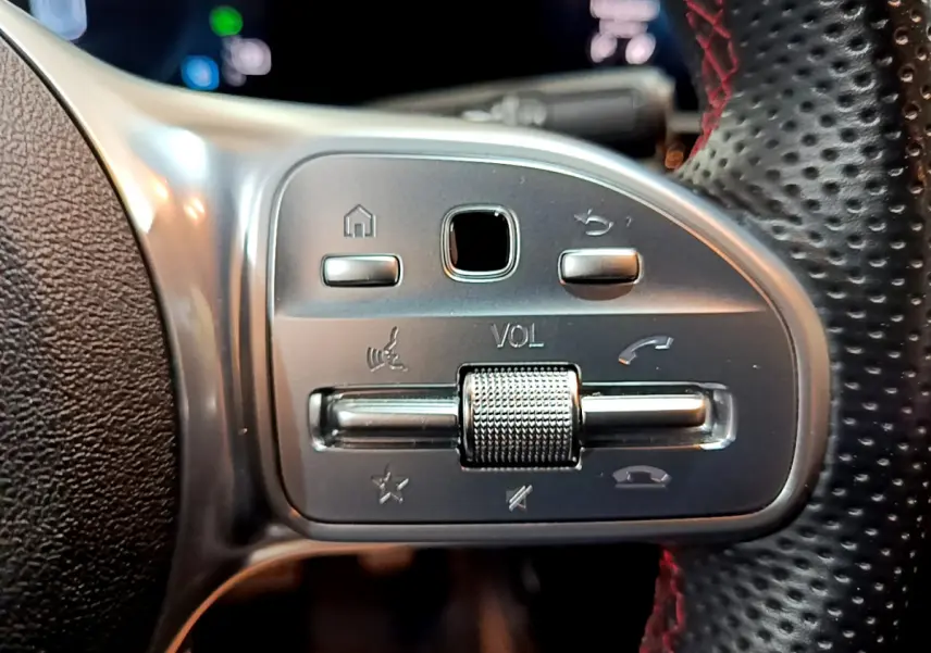 Gros plan sur les commandes de volume et téléphone au volant cuir perforé rouge d'une Mercedes Classe A 180 AMG Line noire.