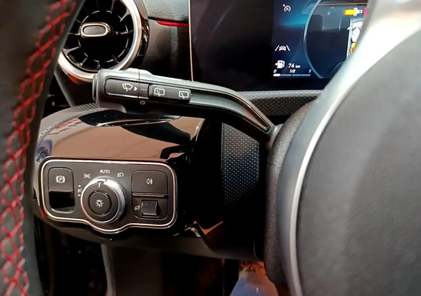 Gros plan sur la commande d’éclairage et le volant cuir noir avec surpiqûres rouges côté gauche d’une Mercedes Classe A A 180 AMG Line 2019.