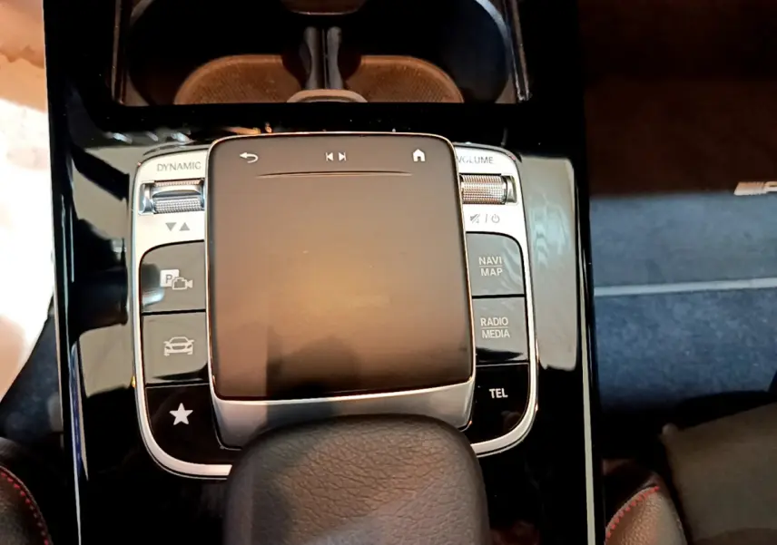 Gros plan sur la console centrale noire brillante de la Mercedes Classe A 180 AMG Line avec pavé tactile et commandes multimédia.