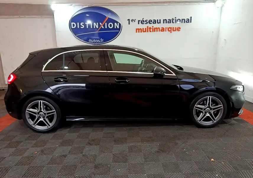 Profil droit d'une Mercedes Classe A 180 AMG Line noire avec jantes alliage cinq branches en intérieur showroom.