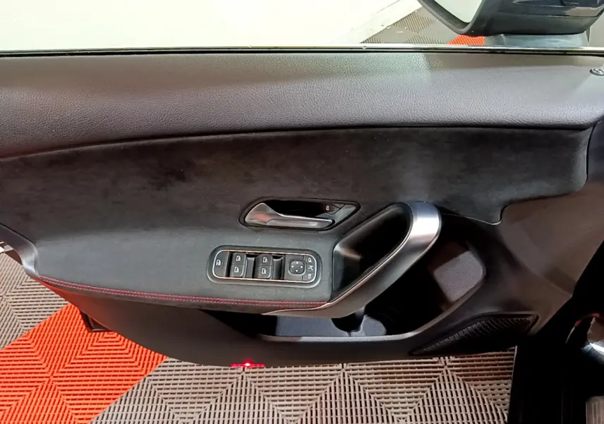 Gros plan sur la porte côté gauche d'une Mercedes Classe A 180 AMG Line noire, avec commandes de vitres et poignée alu.
