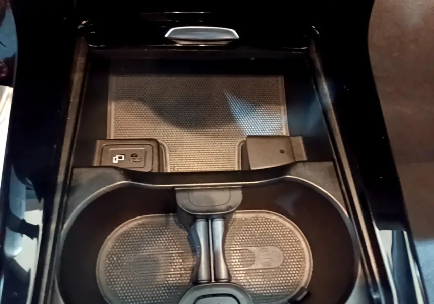 Gros plan sur la console centrale noire de la Mercedes Classe A 180 AMG Line, avec porte-gobelets et recharge sans fil.