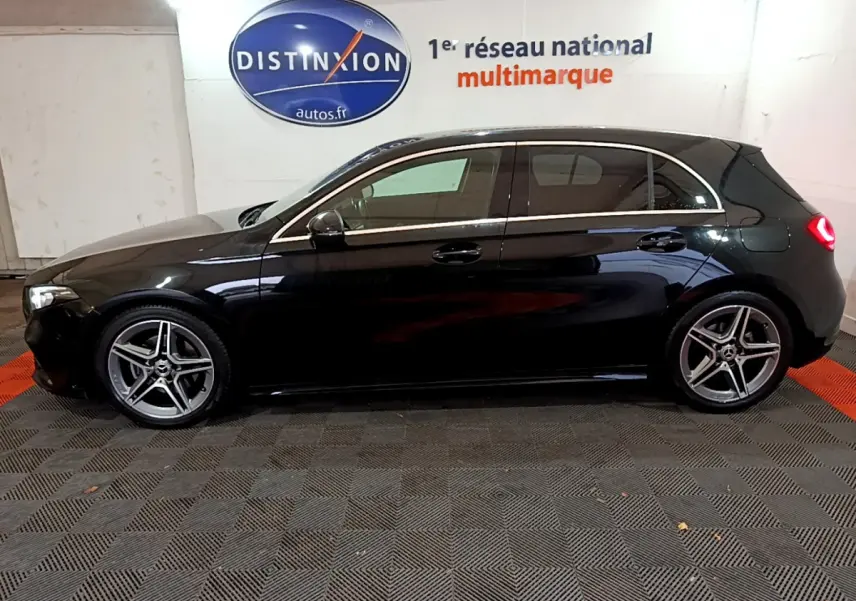Profil droit d'une Mercedes Classe A 180 AMG Line noire, avec jantes alliage et feux arrière allumés dans un showroom.
