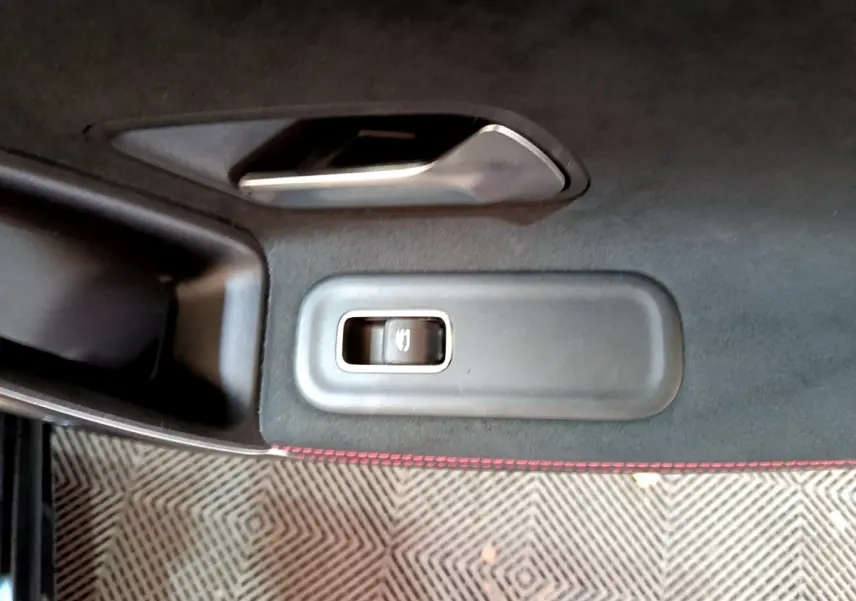 Gros plan sur la commande de lève-vitre côté gauche d'une Mercedes Classe A 180 AMG Line noire, avec surpiqûres rouges.