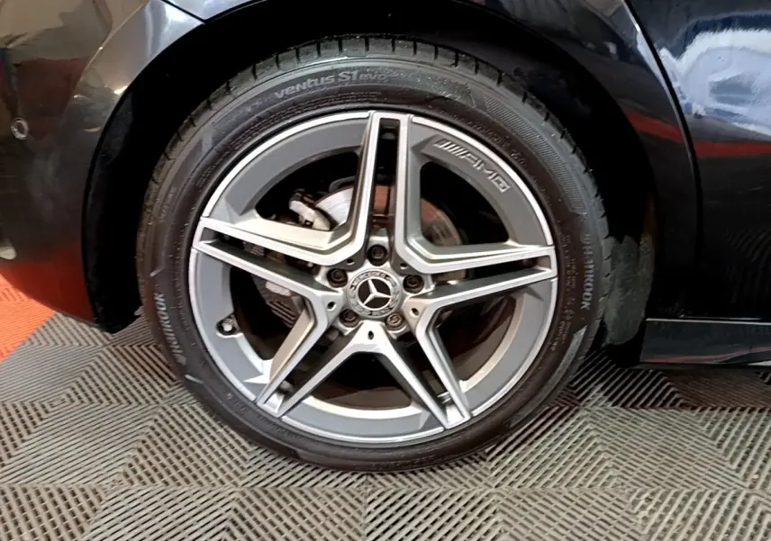 Gros plan sur la roue avant droite noire d'une Mercedes Classe A 180 AMG Line avec jante AMG argentée cinq branches