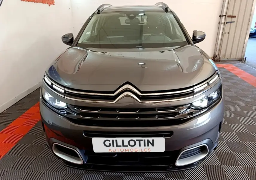 Vue avant d'un Citroën C5 Aircross gris foncé avec feux LED allumés et calandre chromée en intérieur showroom.