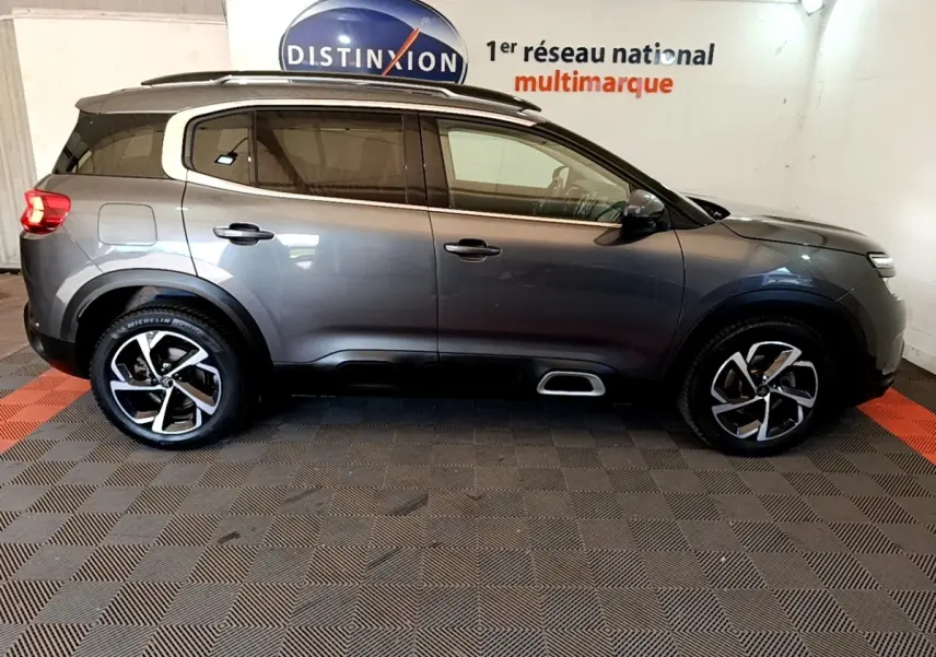 Vue de profil côté gauche d'un Citroën C5 Aircross gris foncé avec jantes alliage et barres de toit chromées.