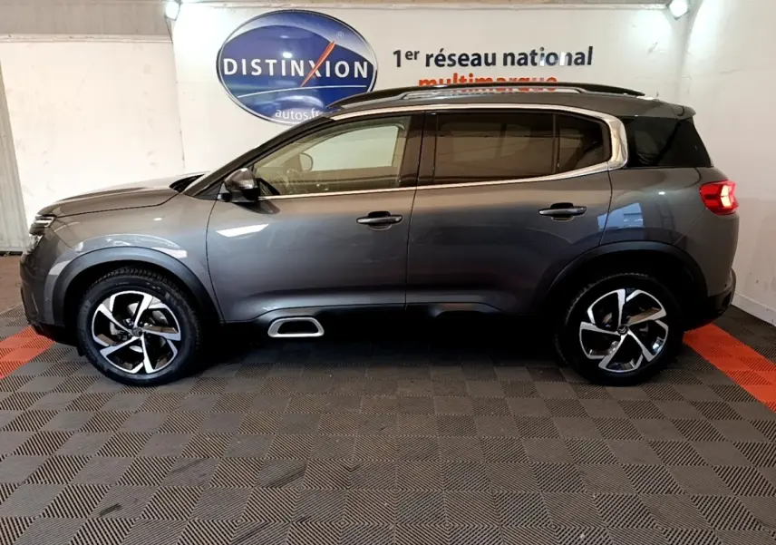 Profil côté gauche d'un Citroën C5 Aircross gris foncé 2020 avec jantes alliage et barres de toit chromées.