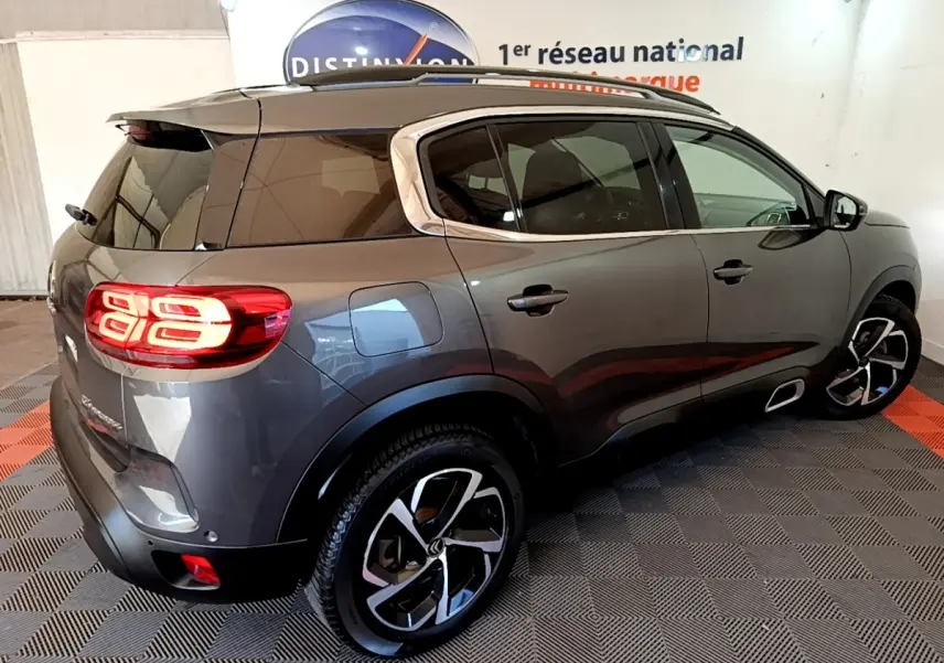 Vue 3/4 arrière droite d'un Citroën C5 Aircross gris foncé avec feux arrière LED allumés et jantes bicolores.