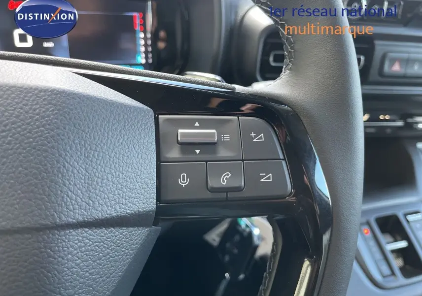 Gros plan sur les commandes au volant cuir noir du Citroën Berlingo 2026, avec tableau de bord numérique en arrière-plan.