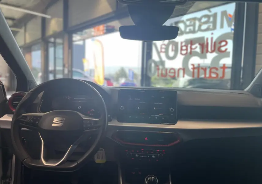 Vue intérieure avant du SEAT Arona 2024 rouge Passion, avec volant sport cuir, écran tactile et détails rouges sur la console.