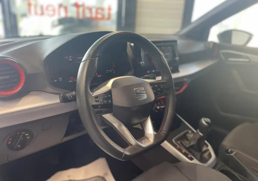 Vue intérieure centrée sur le volant sport cuir avec logo SEAT, tableau de bord digital et levier de vitesse manuel.