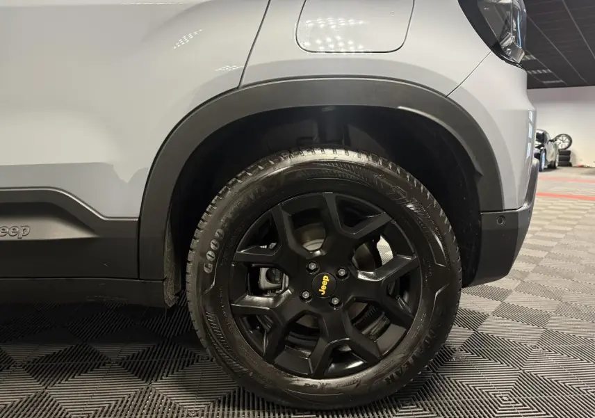 Gros plan sur la roue avant droite noire avec logo Jeep jaune, sur carrosserie gris clair du Jeep Avenger.