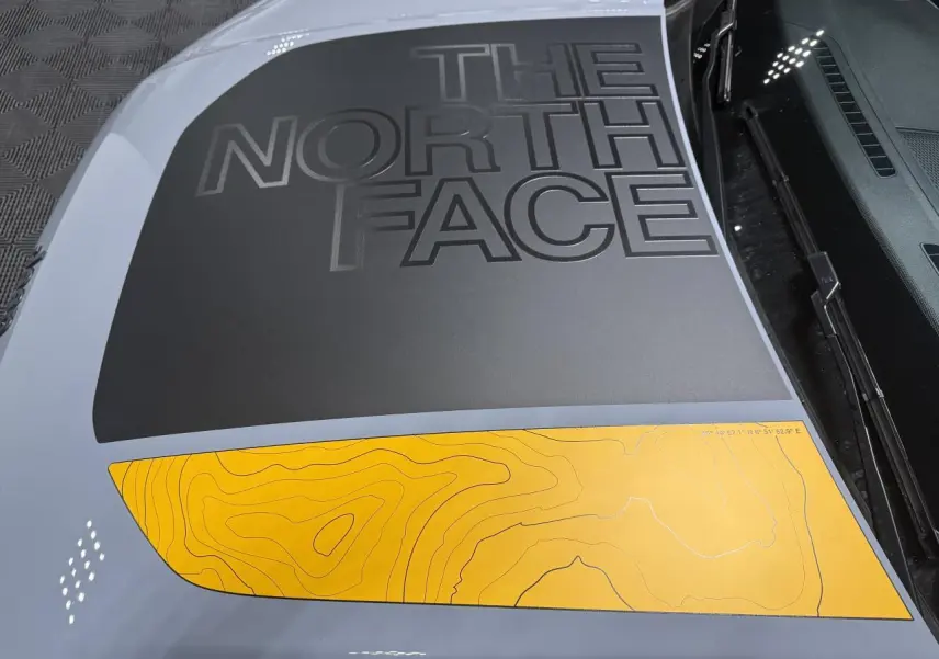 Vue rapprochée du capot gris du Jeep Avenger avec sticker noir "The North Face" et motif topographique jaune.