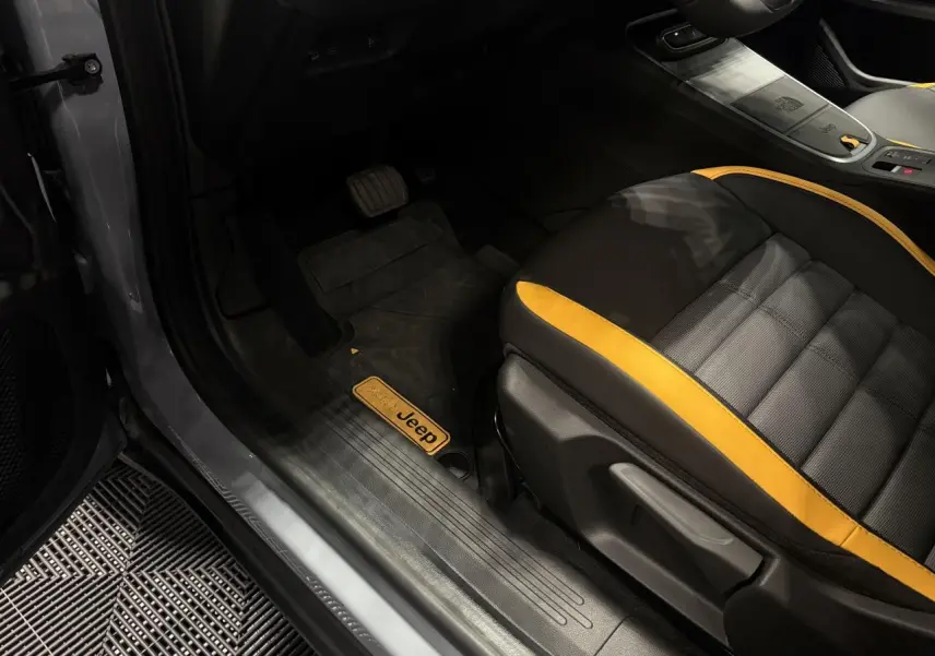 Vue intérieure côté conducteur du Jeep Avenger gris, avec siège noir et jaune et tapis de sol marqué Jeep.