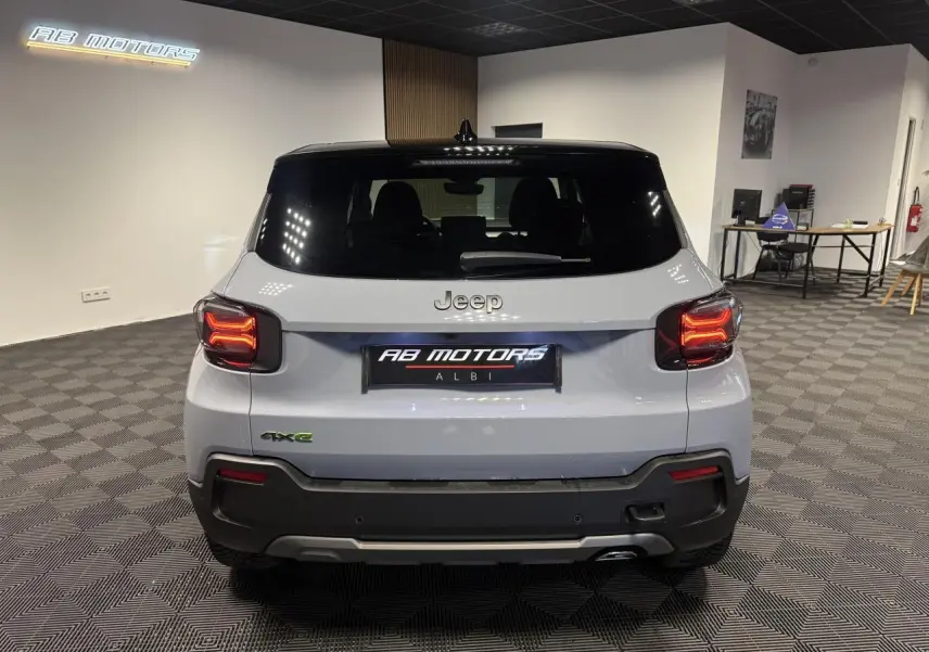 Vue arrière d'un Jeep Avenger gris avec toit noir et feux arrière LED allumés dans un showroom.