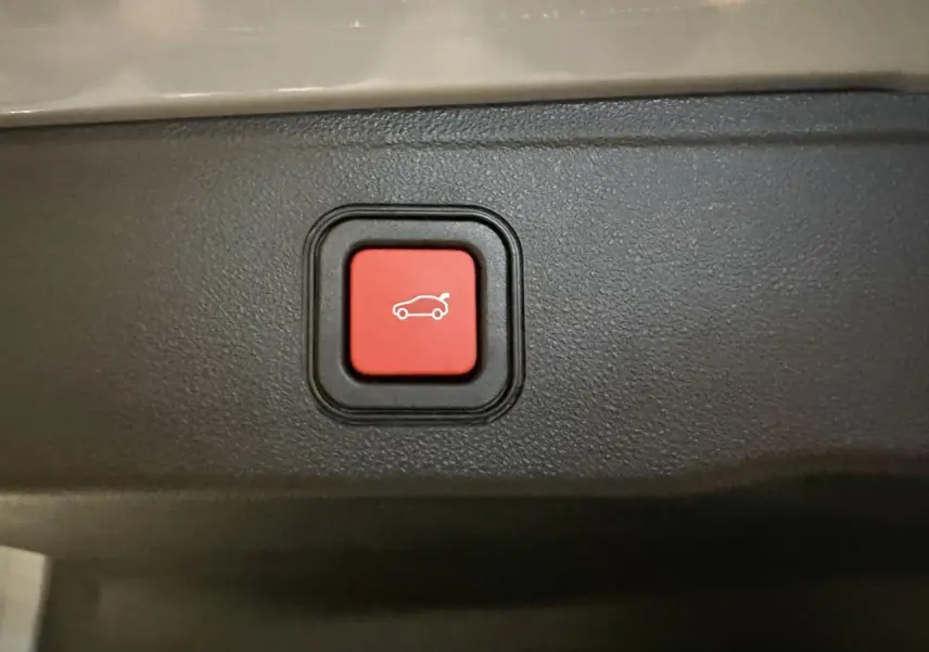 Gros plan sur bouton rouge d'ouverture électrique du coffre dans l'habitacle du Jeep Avenger gris.