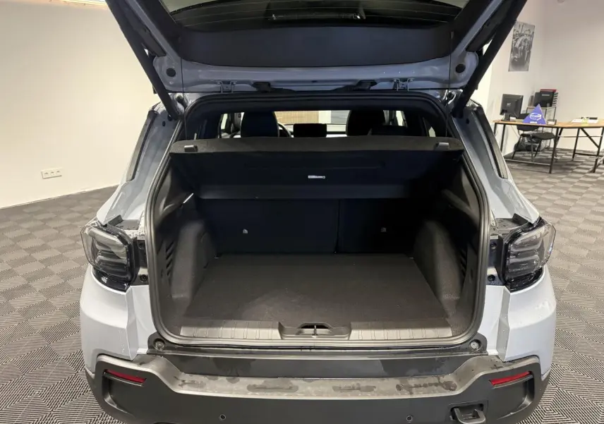 Vue arrière du coffre ouvert d'un Jeep Avenger gris avec toit ouvrant en verre dans un showroom.