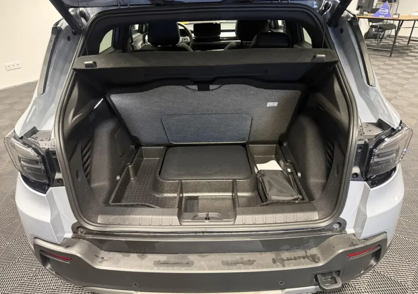 Coffre ouvert vu de l'arrière d'un Jeep Avenger gris avec intérieur de coffre compartimenté et banquette arrière visible.