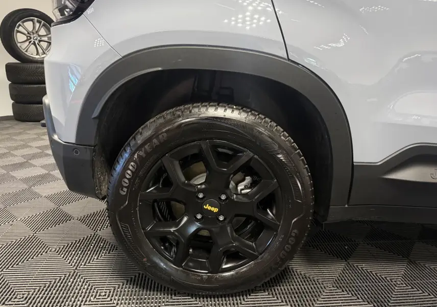Gros plan sur la roue avant gauche noire avec jante alliage Jeep sur carrosserie gris clair du Jeep Avenger Hybrid 4xe.