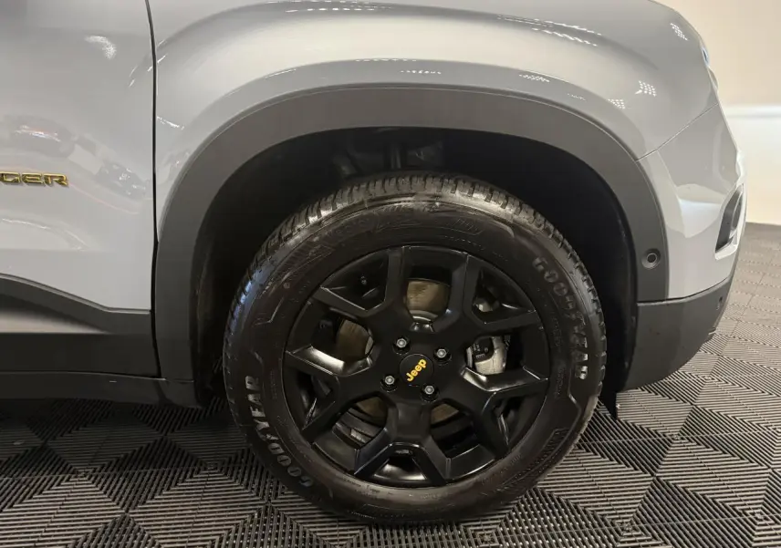 Gros plan sur la roue avant droite noire mat d’un Jeep Avenger gris avec badge jaune et jante 17 pouces.