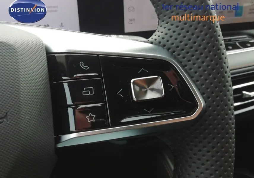 Gros plan sur les commandes gauche du volant perforé noir du MG MOTOR EHS blanc perle, avec écran tactile en arrière-plan.