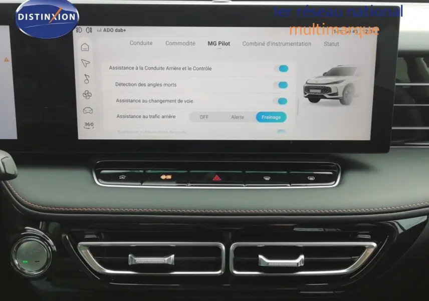 Vue rapprochée de l’écran tactile central et de la console noire du MG MOTOR EHS 1.5T PHEV 272CH LUXURY blanc perle, affichant les assistances à la conduite.