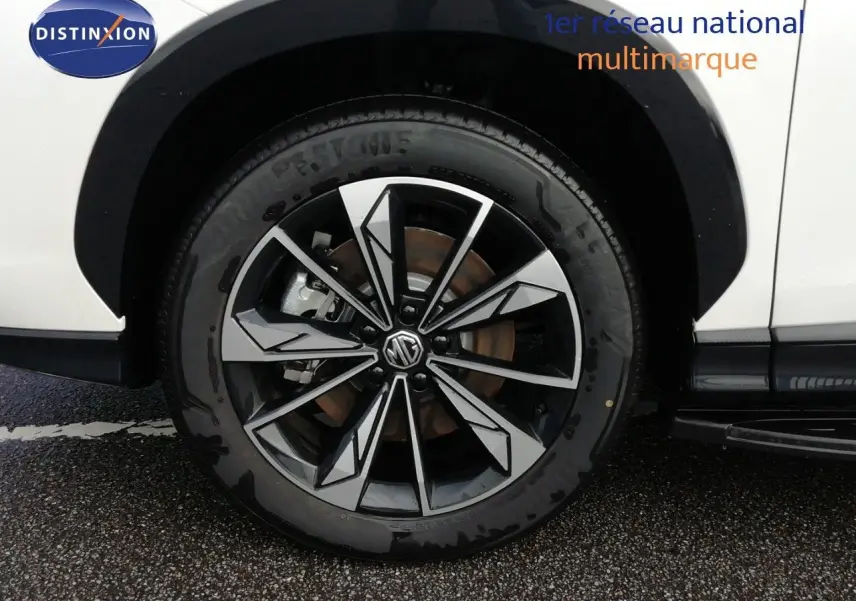 Gros plan sur la roue avant droite d’un MG MOTOR EHS 1.5T PHEV 272CH Luxury blanc nacré avec jante alliage bicolore.