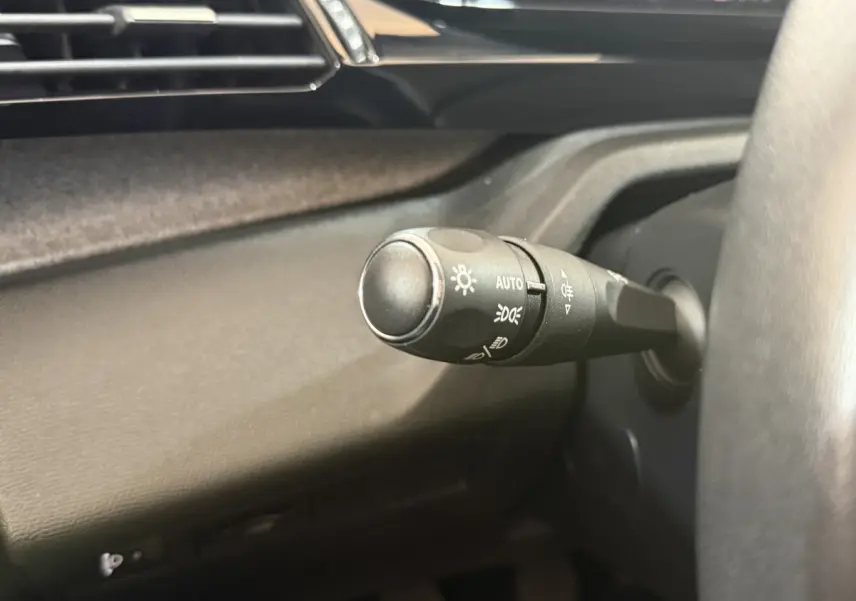 Gros plan sur la commande d'éclairage à gauche du volant dans l'habitacle sombre d'une Peugeot 308 2023 bleu.