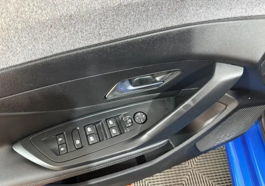 Vue intérieure côté gauche de la porte d’une Peugeot 308 bleu 2023, avec commandes des vitres et rétroviseurs électriques.