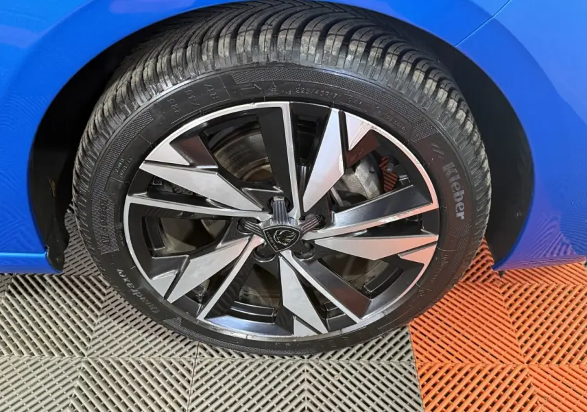 Gros plan sur la roue avant gauche d'une Peugeot 308 bleu 2023 avec jante alliage bicolore moderne