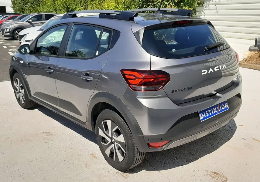 Vue 3/4 arrière droite d'une Dacia Sandero Stepway gris schiste avec barres de toit et feux arrière LED.