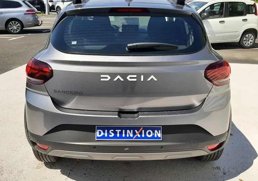 Vue arrière d'une Dacia Sandero Stepway gris schiste 2025 avec feux rouges et logo distinctif sur parking.