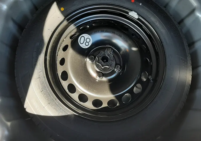 Gros plan sur la roue de secours noire avec étiquette de vitesse 80 km/h, logée dans le coffre du Dacia Sandero Stepway gris schiste.
