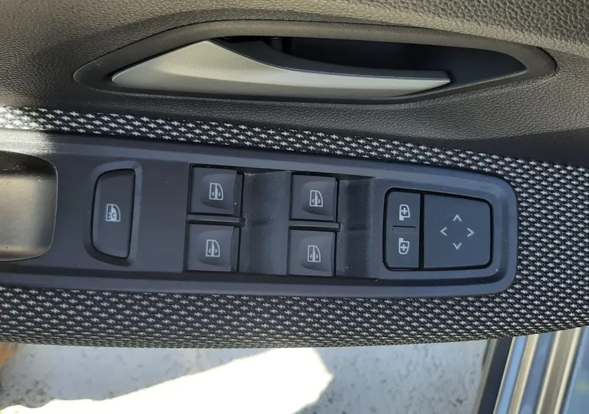 Gros plan sur la commande des vitres et rétroviseurs côté conducteur, garniture tissu gris à motifs sur porte Dacia Sandero Stepway.