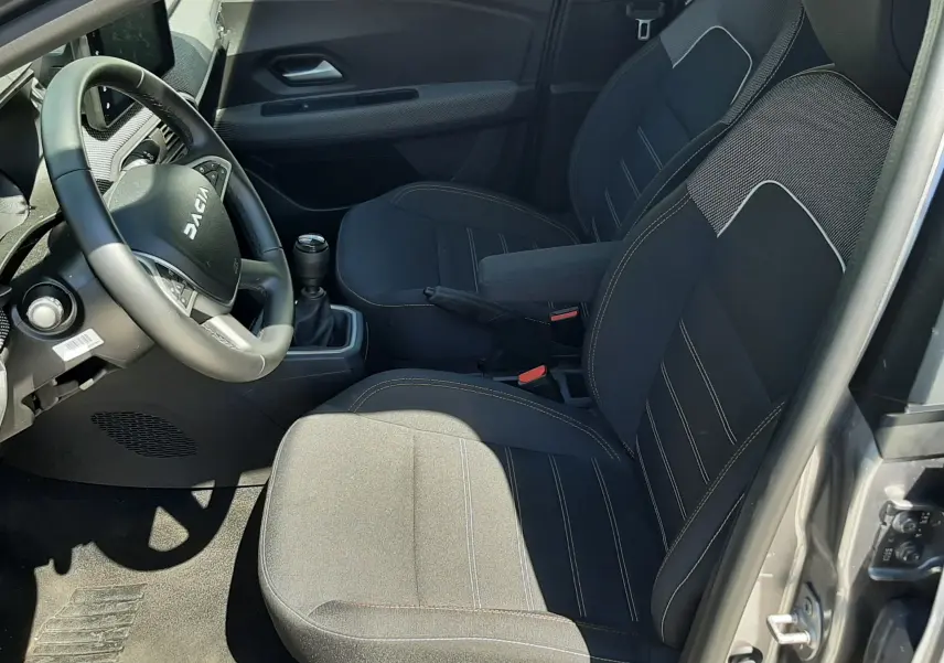 Vue intérieure côté conducteur de la Dacia Sandero Stepway 2025, sièges tissu gris avec volant multifonction et boîte manuelle.