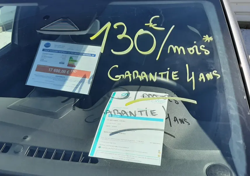 Vue avant rapprochée d'une Dacia Sandero Stepway gris schiste avec inscription jaune "130€/mois Garantie 4 ans" sur le pare-brise.
