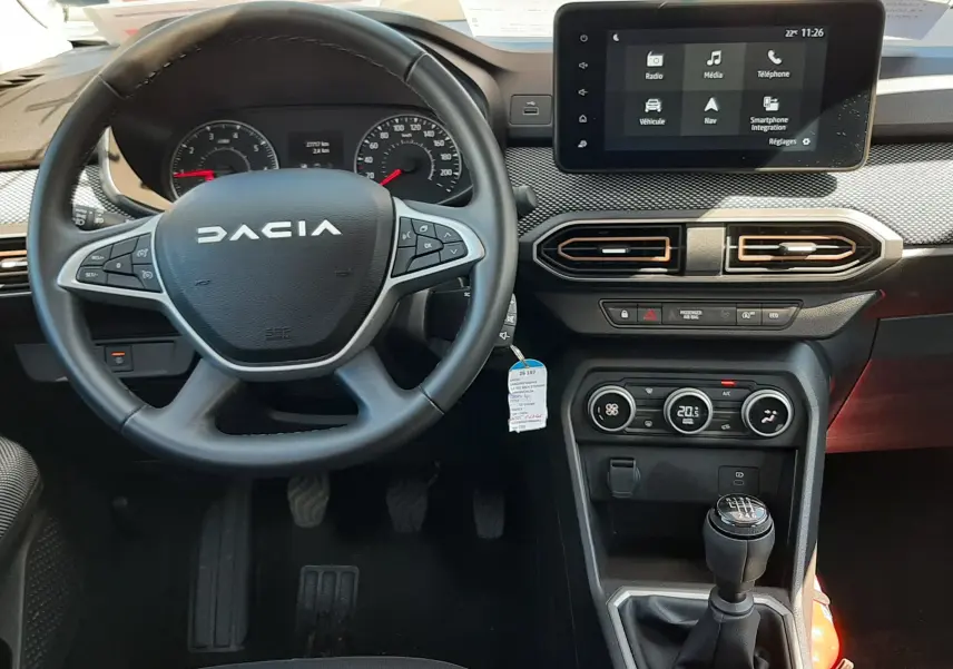 Intérieur de la Dacia Sandero Stepway 2025, vue centrée sur le volant, tableau de bord et écran tactile, ambiance gris foncé.