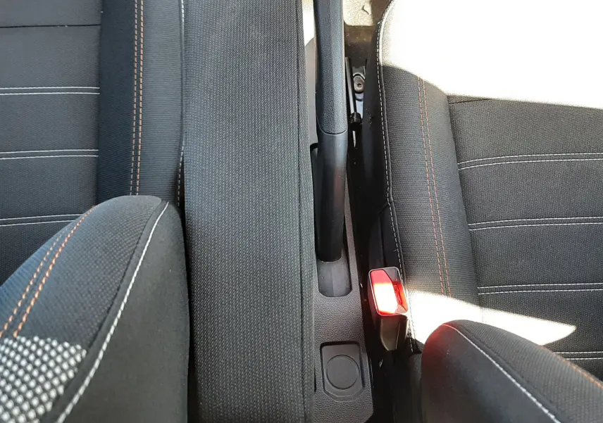 Vue plongeante sur l'accoudoir central et frein à main entre les sièges avant en tissu gris foncé de la Dacia Sandero Stepway 2025.
