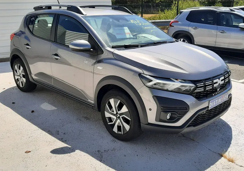 Vue 3/4 avant droite d'une Dacia Sandero Stepway gris schiste avec barres de toit et jantes alliage distinctives.