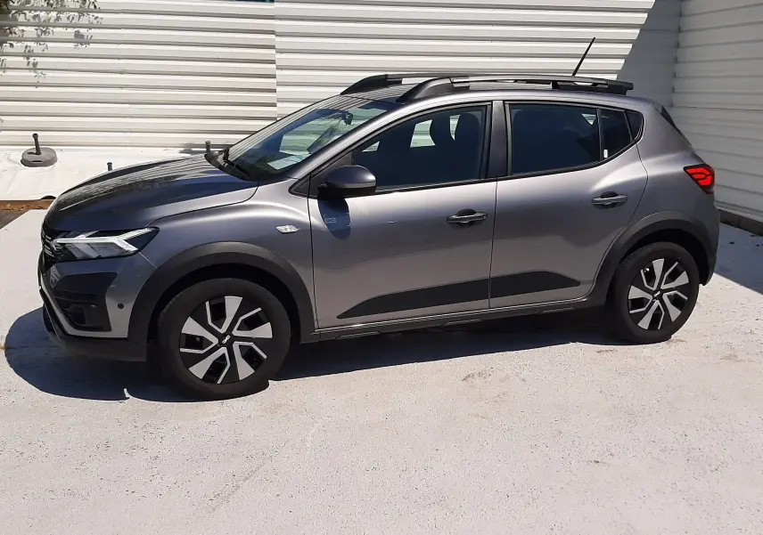 Profil droit d'une Dacia Sandero Stepway gris schiste 2025 avec barres de toit et jantes spécifiques, stationnée en extérieur.