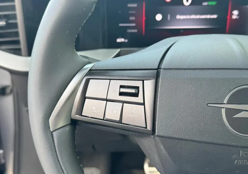 Gros plan sur le volant gris de l’Opel Mokka électrique 2025, avec commandes intégrées et logo Opel visible.