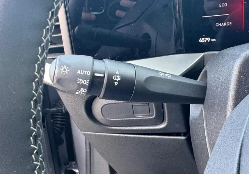 Gros plan sur le commodo gauche du volant d’un Opel Mokka électrique gris, affichage digital partiel en arrière-plan.