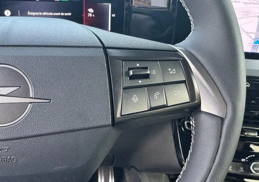 Gros plan sur le volant noir de l’Opel Mokka électrique 2025 avec commandes intégrées et logo Opel visible.