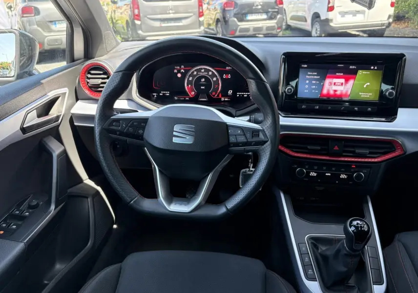 Vue intérieure frontale du volant sport cuir et tableau de bord digital du SEAT Arona 2024 avec touches rouges et levier de vitesse manuel.