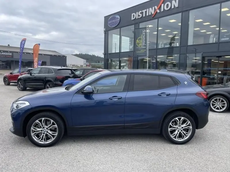 Vue de profil côté gauche d’un BMW X2 bleu métal 2021 stationné devant un showroom Distinxion.